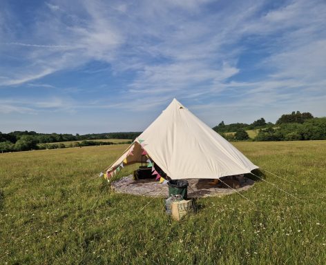 Meet and Greet Tipi Tent A bell tent set up in a grassy field under a blue sky with wispy clouds.